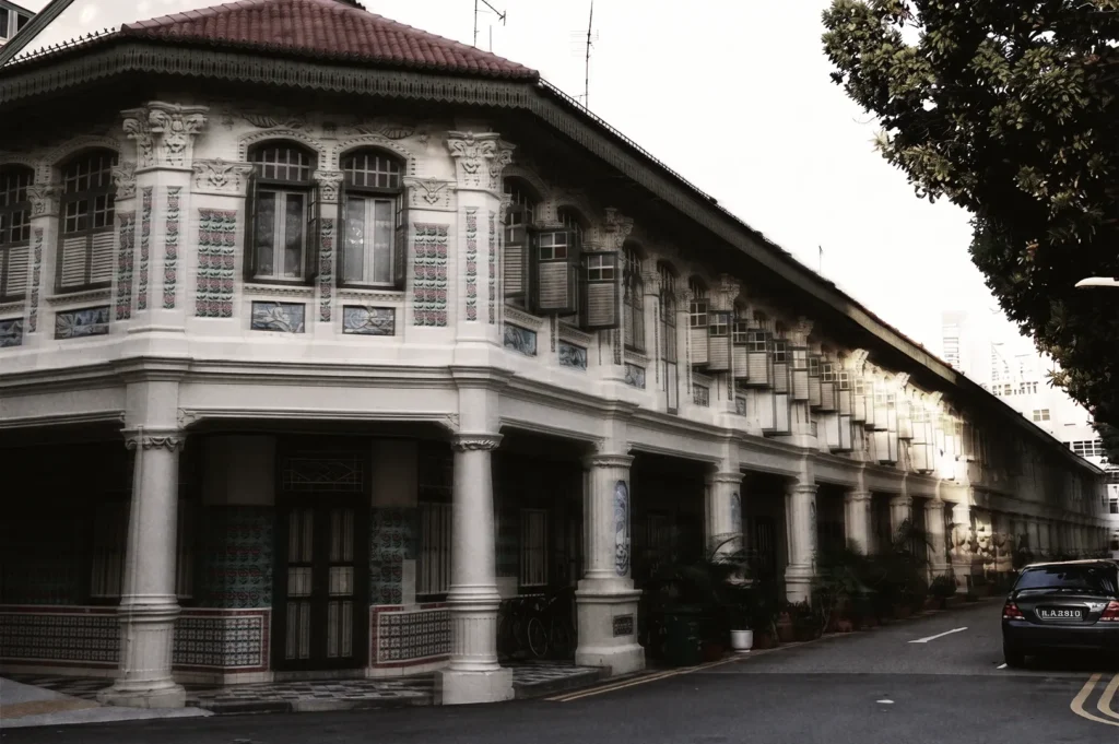Historic Peranakan-style shophouse building with ornate decorative tiles, classical pillars, shuttered windows, and a black car parked on the street.