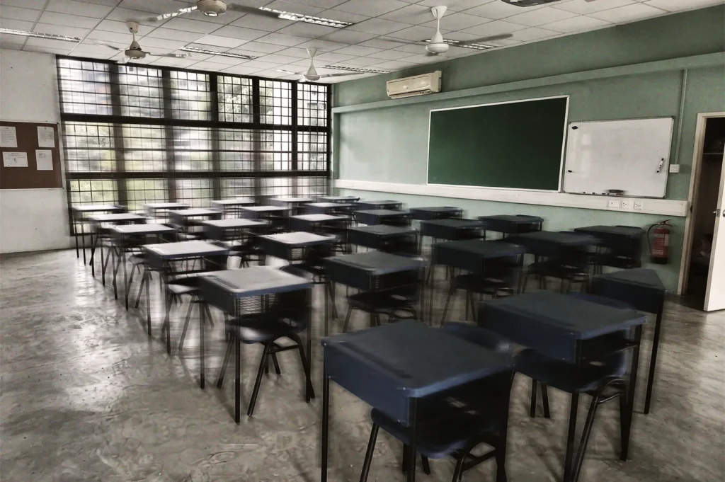 Neatly arranged desks and chairs in a bright classroom with large windows, green chalkboard, and whiteboard, representing education and learning spaces.